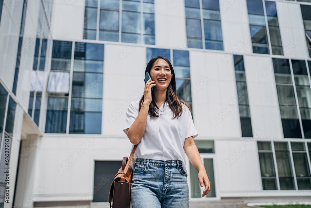 Young busy successful beautiful Japanese business woman, Japanese professional businesswoman holding cellphone using smartphone standing or walking on big city urban street outside