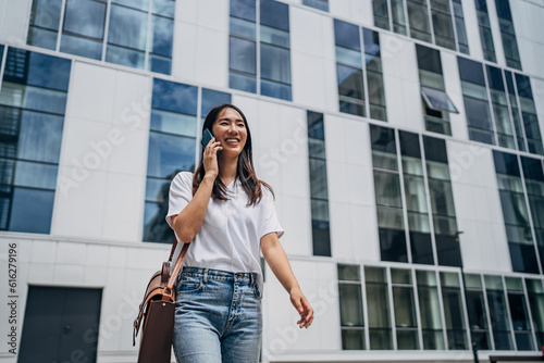 Young busy successful beautiful Japanese business woman, Japanese professional businesswoman holding cellphone using smartphone standing or walking on big city urban street outside