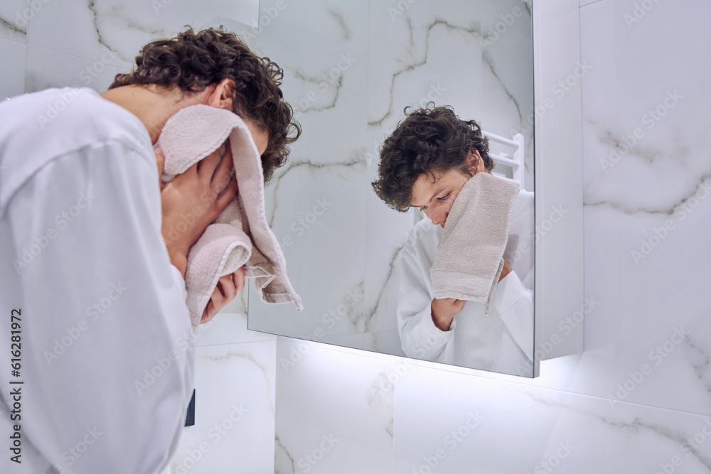 Young guy in bathroom near mirror washing face, wiping with towel Young guy in bathroom near mirror washing face, wiping with towel