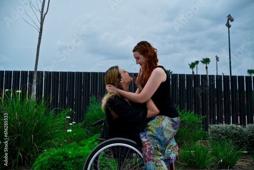 Fotografi Loving woman sitting on knees of girlfriend with disability