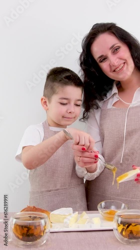 mom and little son spread on cheese honey breakfast healthy food on white background drink tea kitchen apron photo