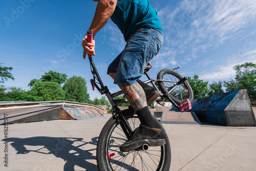 An unrecognizable oldish tattooed freestyle bmx rider is performing tricks in a skate park.