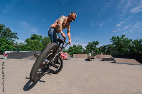 Wide angle view of an urban shirtless mature man doing extreme sports on his bmx in a skate park.