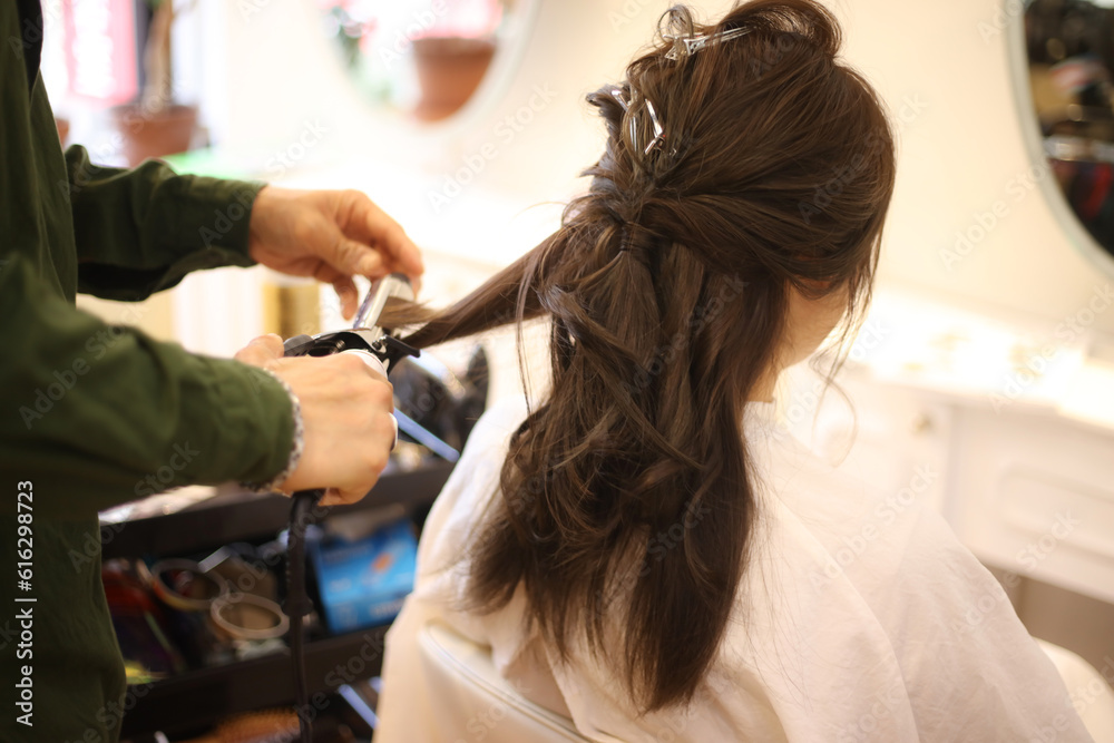 女性の髪にヘアアイロンをかける男性美容師 女性の髪にヘアアイロンをかける男性美容師