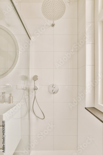 a white bathroom with a shower head and hand held in front of the mirror above it is an image of a large round mirror