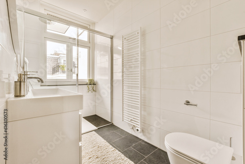 a white bathroom with black tile flooring and a toilet in the corner  next to a window that looks out onto the street