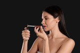 Woman using long cigarette holder for smoking on black background, space for text