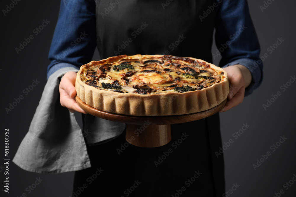 Woman holding delicious quiche with mushrooms on dark grey background, closeup