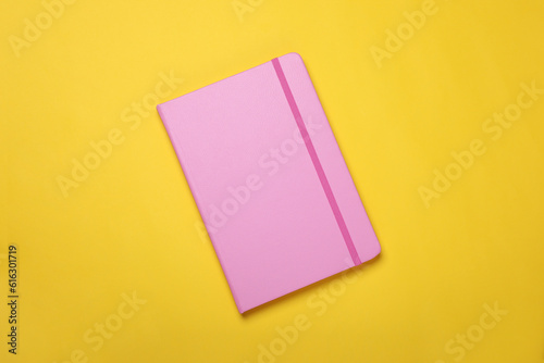 Closed pink notebook on yellow background, top view