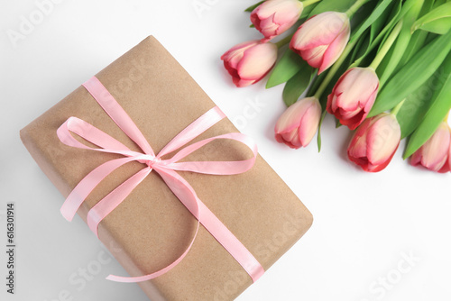 Beautiful gift box with bow and pink tulips on white background, flat lay