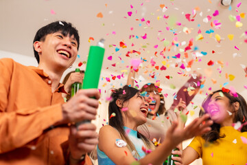 Group of Happy young Asian man and woman friends college student enjoy and fun celebration holiday event meeting party dancing and playing paper shoot together in living room at home on vacation night