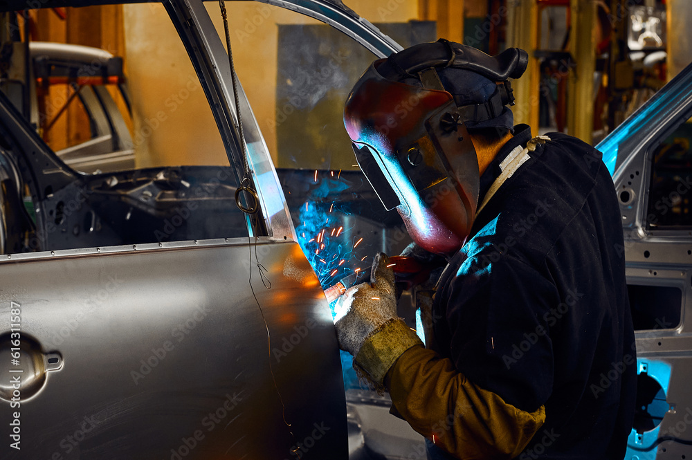 Welder in helmet works with metal parts of car carcass
