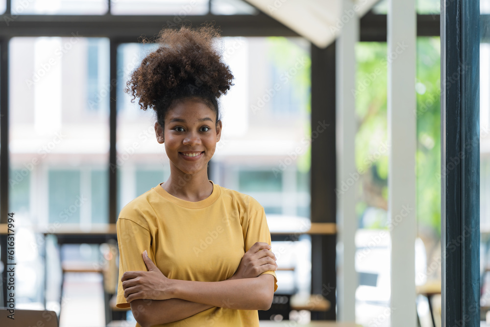 Young pretty African American standing and arms crossed near a window. Young pretty African American standing and arms crossed near a window.