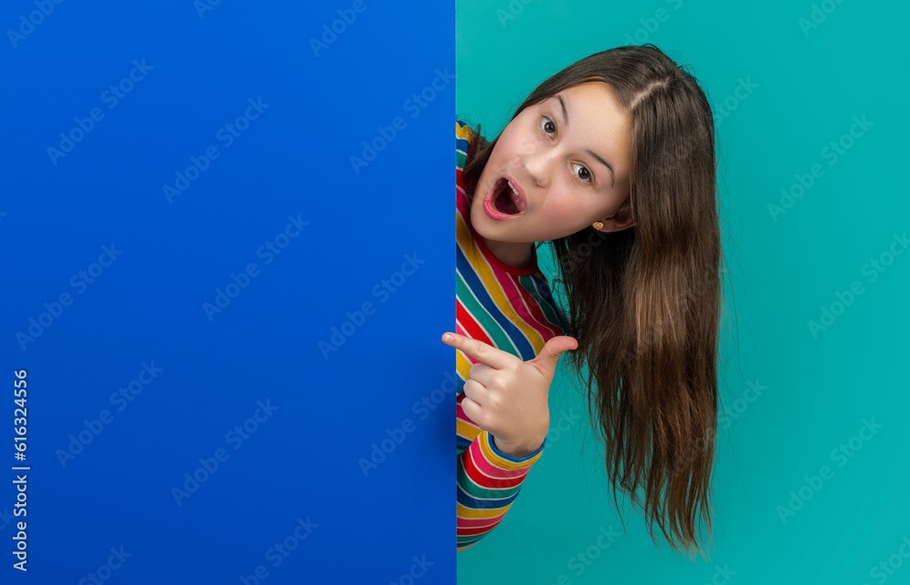 amazed kid behind blank blue paper with copy space for advertisement. point finger amazed kid behind blank blue paper with copy space for advertisement. point finger