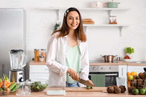 Young woman cutting cucumber for vegetable juice in kitchen