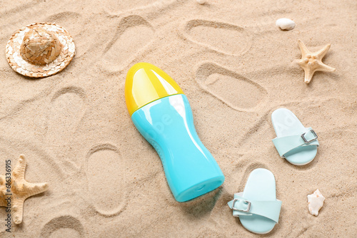 Creative composition with sunscreen cream, flip flops and summer hat on sand
