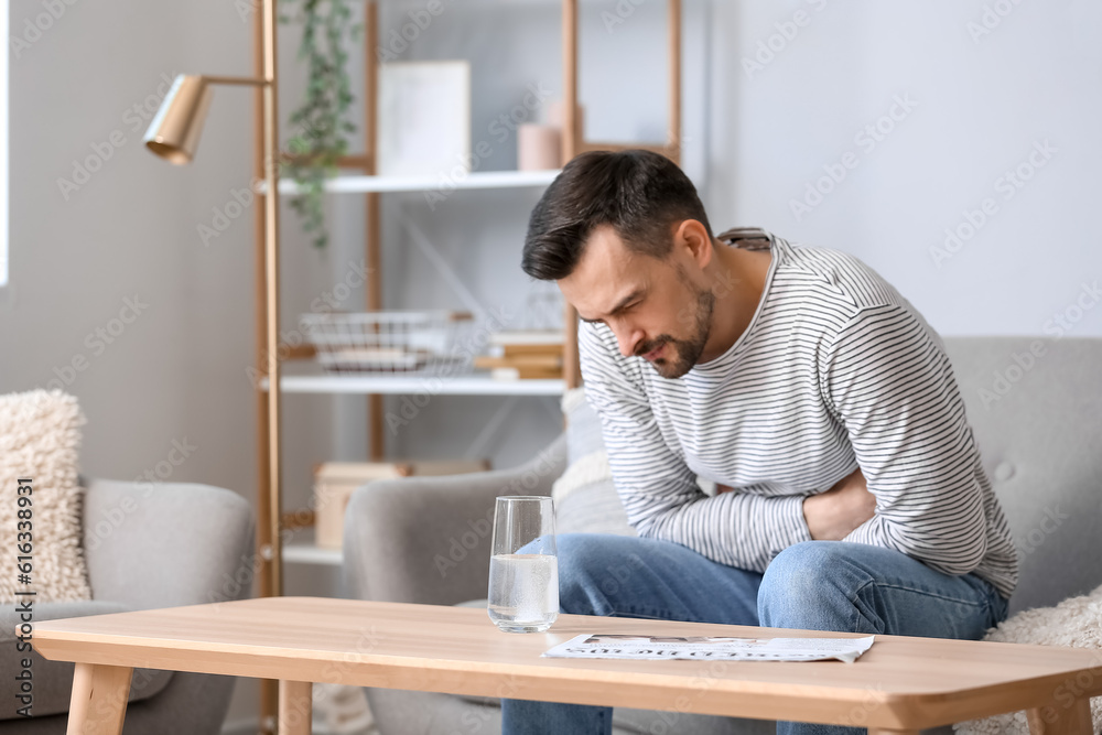 Young man with soluble tablet in glass of water suffering from bellyache at home Young man with soluble tablet in glass of water suffering from bellyache at home