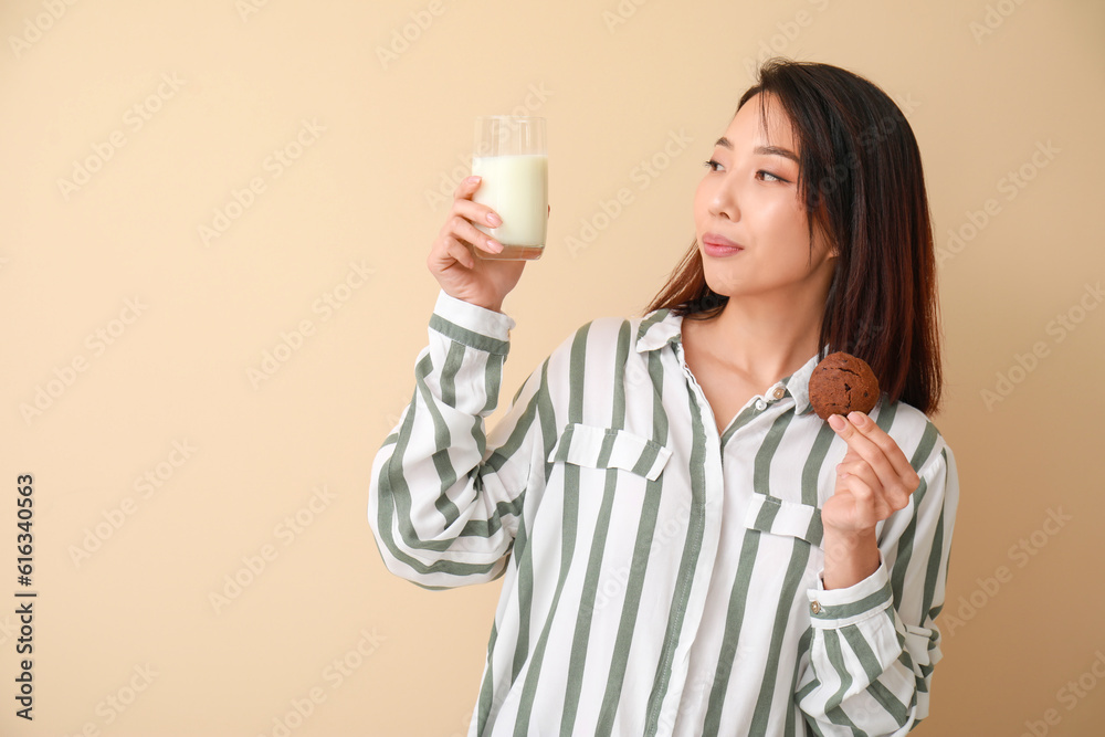 Young Asian woman with milk and cookie on beige background Young Asian woman with milk and cookie on beige background