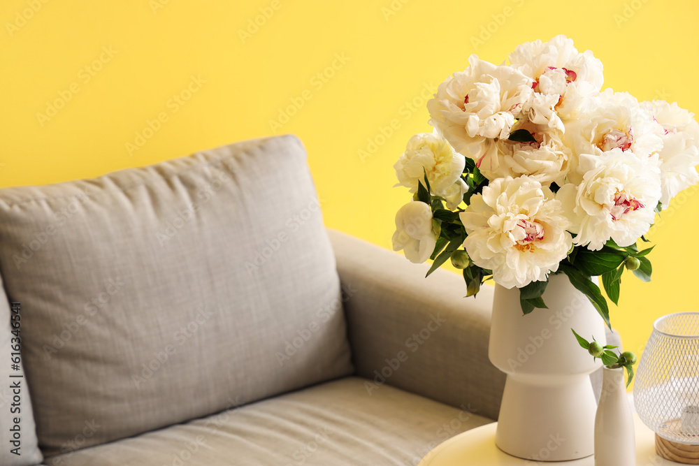 Vase of white peonies with coffee table and couch near yellow wall Vase of white peonies with coffee table and couch near yellow wall