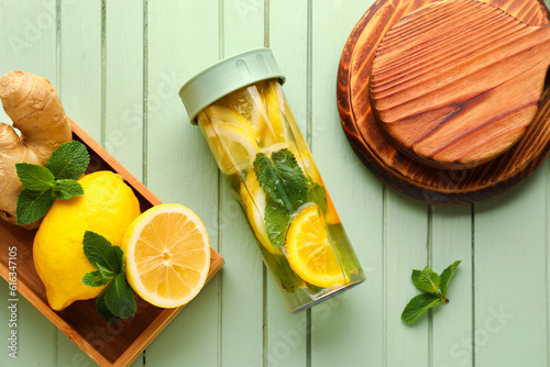 Sports bottle of infused water and box with lemon on green wooden background