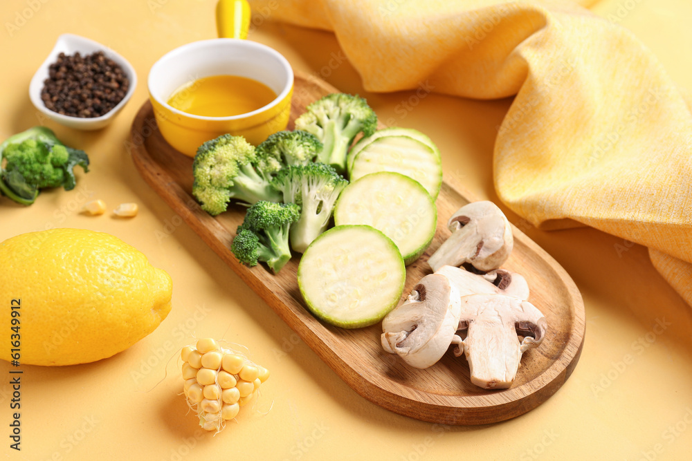 Wooden board with fresh vegetables on yellow background Wooden board with fresh vegetables on yellow background