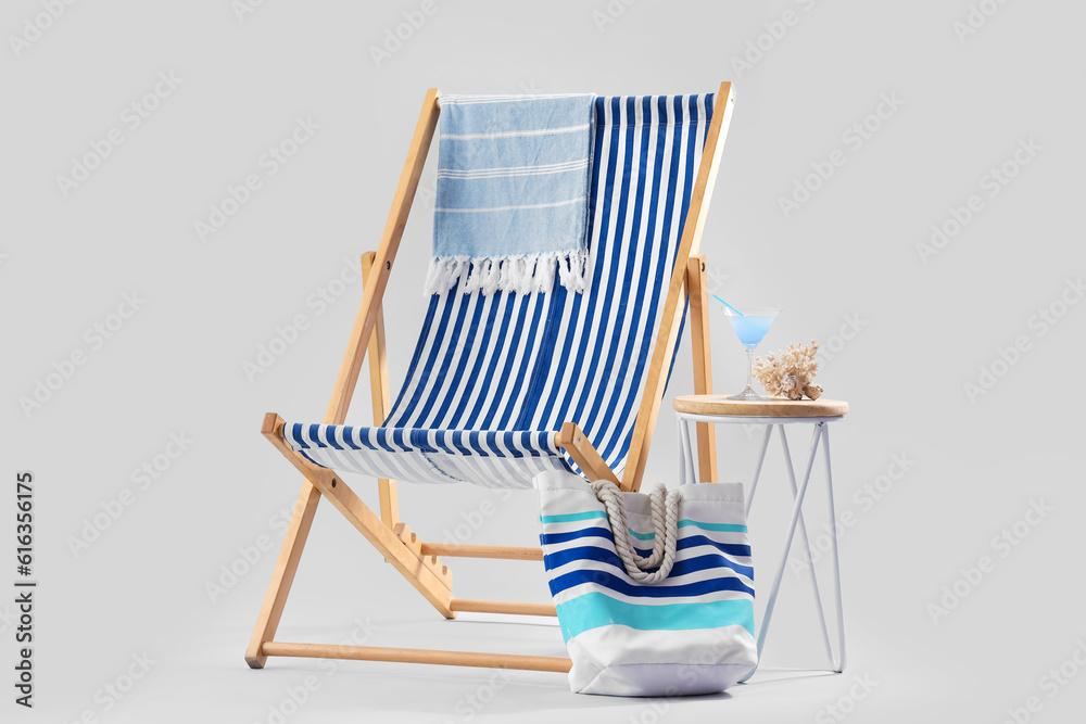 Deckchair with beach accessories, cocktail and coral on stool against grey background