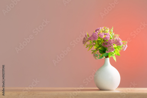 pink spirea in white vase on wooden shelf