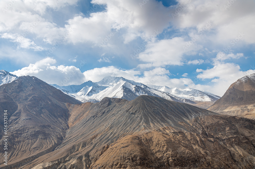 The barren landscape of Leh, Ladakh. Landscape view of rocky land surrounded by snow-covered Himalayas and Dramatic clouds.