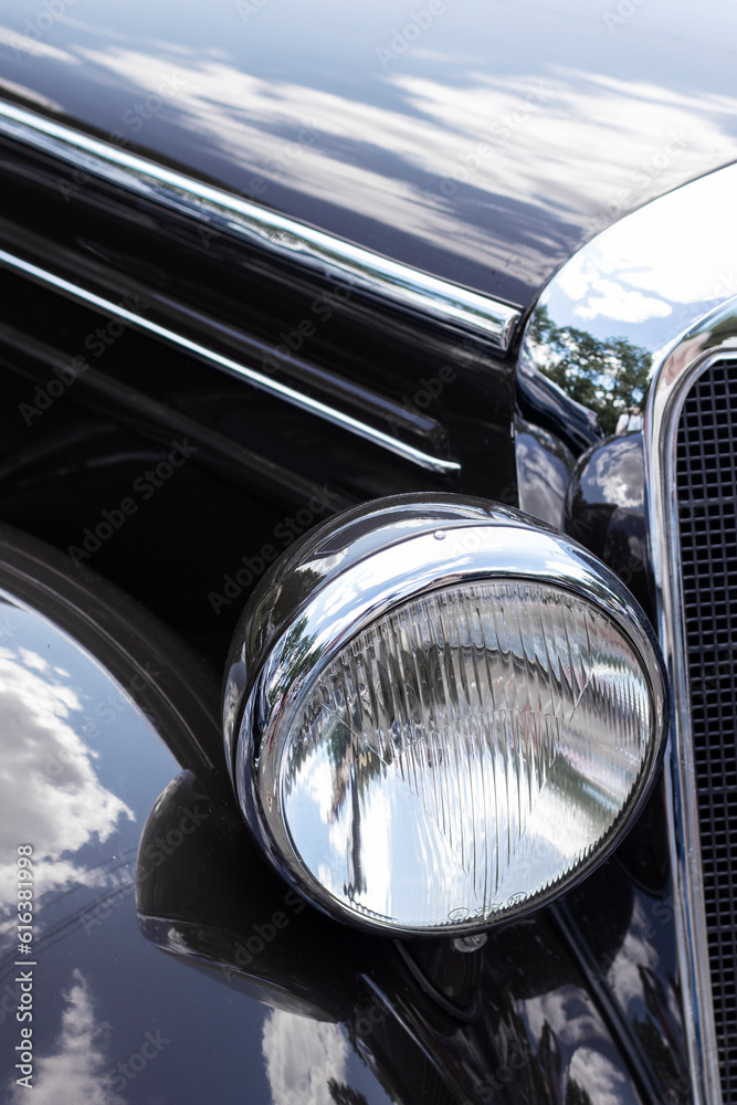 Chrome headlight on a black retro car. Close up.