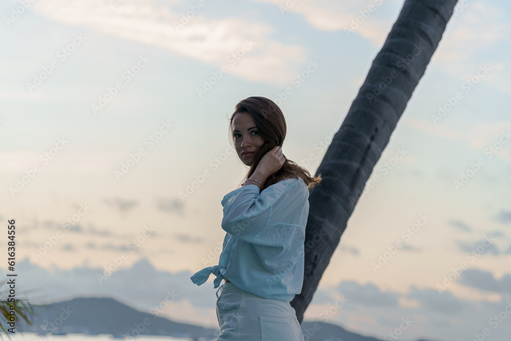 portrait of brunette girl standing at dawn against a palm tree by the ocean. The scattered light, the morning glow, and the start of a new day capture the essence of nature, camping, and summer travel portrait of brunette girl standing at dawn against a palm tree by the ocean. The scattered light, the morning glow, and the start of a new day capture the essence of nature, camping, and summer travel