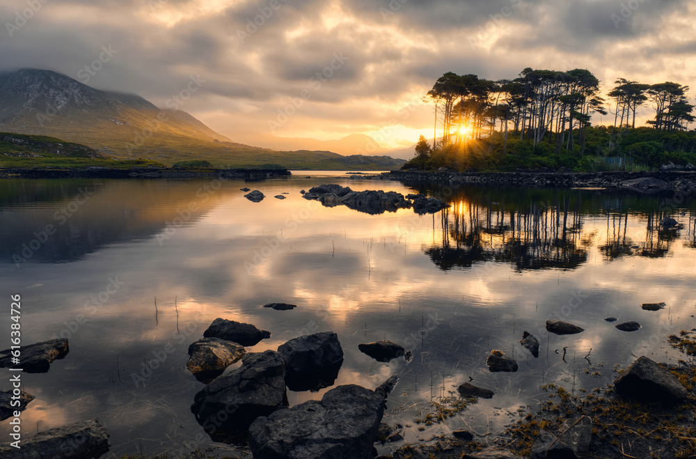 Dramatic cloudy sunrise lakeside landscape scenery of twelve pines island reflected in water surrounded by mountains at Derryclare, connemara national Park in County Galway, Ireland
