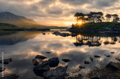 Obraz na płótnie Dramatic cloudy sunrise lakeside landscape scenery of twelve pines island reflected in water surrounded by mountains at Derryclare, connemara national Park in County Galway, Ireland w salonie
