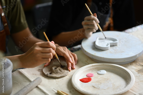 Cropped of two creative men painting pottery plate in workshop. Indoors lifestyle activity and hobbies concept