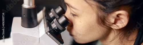 Asian lady doctor looks into contemporary microscope researching sample on slide in hospital