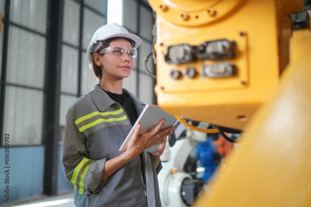 Female Automotive Engineer Wearing Hard Hat, Standing, Using Laptop. Monitoring, Control, Equipment Production. Automated Robot Arm Assembly Line Manufacturing Electric Vehicle Female Automotive Engineer Wearing Hard Hat, Standing, Using Laptop. Monitoring, Control, Equipment Production. Automated Robot Arm Assembly Line Manufacturing Electric Vehicle
