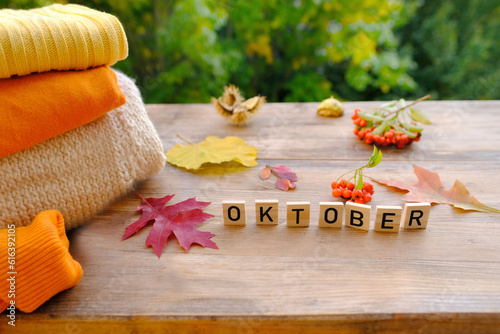 Autumn composition on rustic wooden table in garden with clothing items, fallen yellow, orange leaves and berries, concept happy Thanksgiving, outdoor tea party, good weather, cozy mood, hello autumn