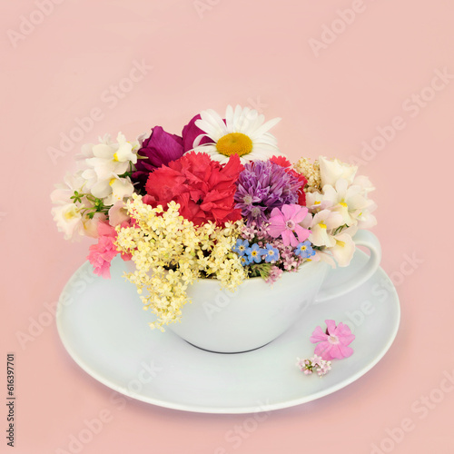 Surreal summer flowers and wildflowers teacup composition on pink background with scattered flowers. Abstract fun health food floral medicinal nature surrealism design.