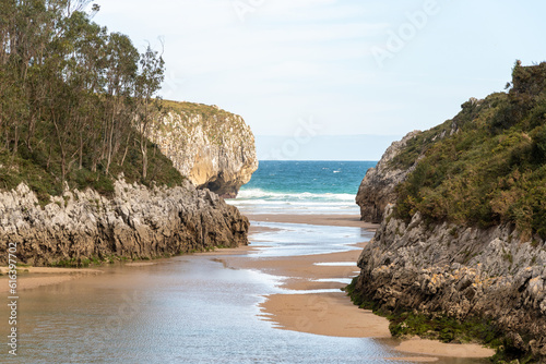 Panoramic view of the tourist beach of Guadamia on the coast of Asturias at low tide with its golden sand and surrounded by vegetation and cliffs on a sunny day. photo