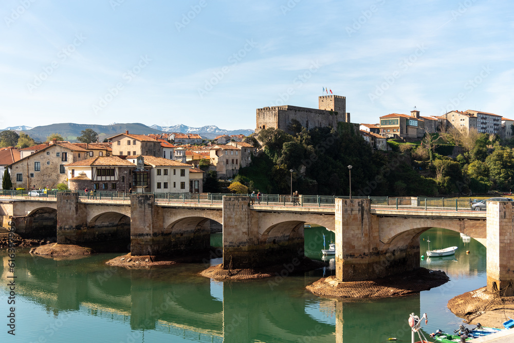 Panoramic view of the medieval stone bridge of the tourist village of San Vicente de la Barquera with the calm sea and surrounded by a natural fishing landscape in Cantabria.