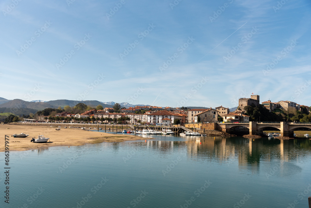 Obraz premium Panoramic view of the tourist village of San Vicente de la Barquera with an impressive stone bridge. Low tide, colourful fishing boats and small houses on a sunny day in Cantabria.