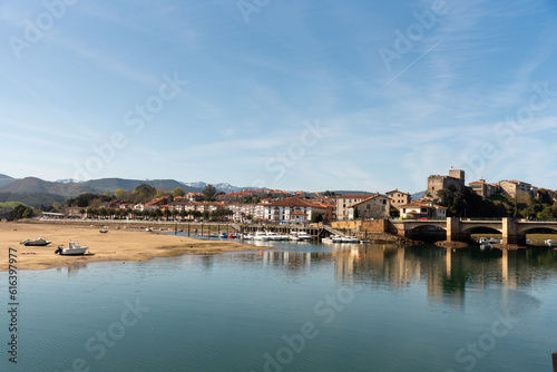 Panoramic view of the tourist village of San Vicente de la Barquera with an impressive stone bridge. Low tide, colourful fishing boats and small houses on a sunny day in Cantabria.