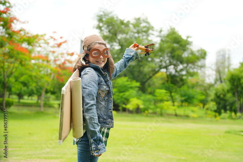 Portrait of red hair kid in pilot costume holding wooden plane running in summer field