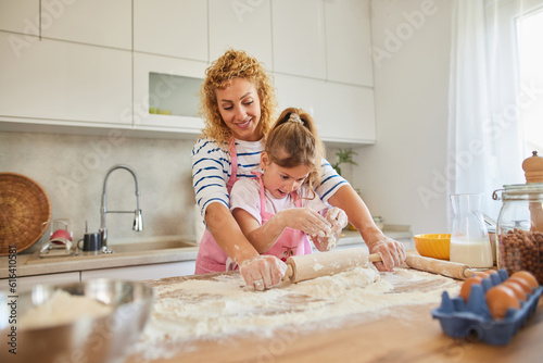 Mother and daughter kneading cookie dough with rolling pin at home