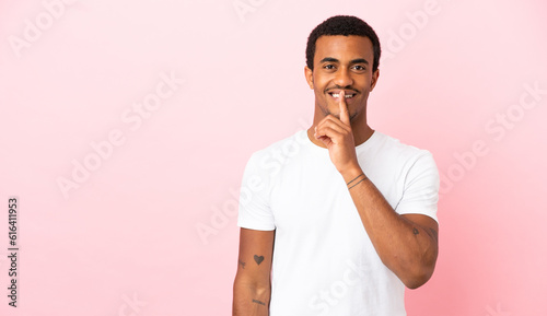 African American man on copyspace pink background showing a sign of silence gesture putting finger in mouth © luismolinero
