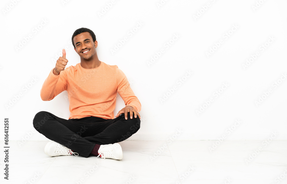 African American man sitting on the floor over isolated copyspace background with thumbs up because something good has happened
