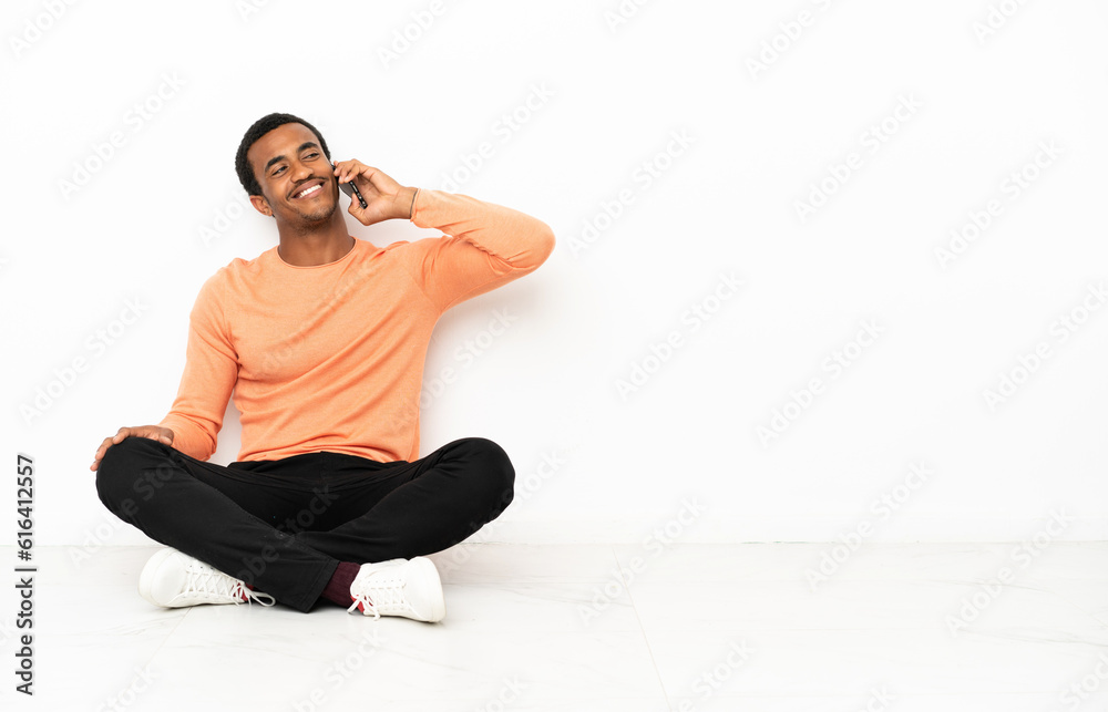 Fototapeta premium African American man sitting on the floor over isolated copyspace background keeping a conversation with the mobile phone