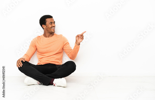 African American man sitting on the floor over isolated copyspace background pointing finger to the side and presenting a product