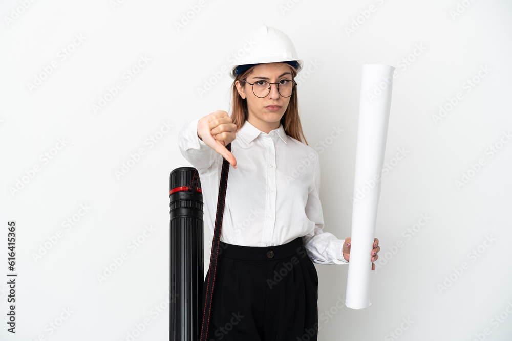 Young architect woman with helmet and holding blueprints isolated on white background showing thumb down with negative expression Young architect woman with helmet and holding blueprints isolated on white background showing thumb down with negative expression