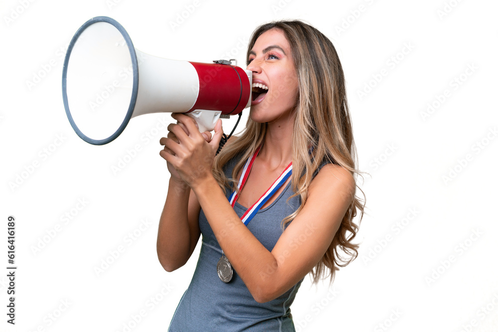 Young pretty sport Uruguayan woman with medals over isolated background shouting through a megaphone Young pretty sport Uruguayan woman with medals over isolated background shouting through a megaphone