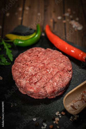 Raw beef hamburger patties with herbs and spices on dark wooden plate